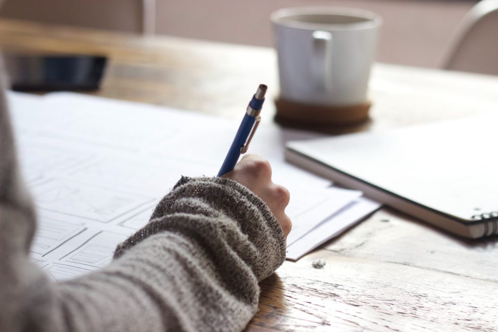 Person in sweater writing in a notebook