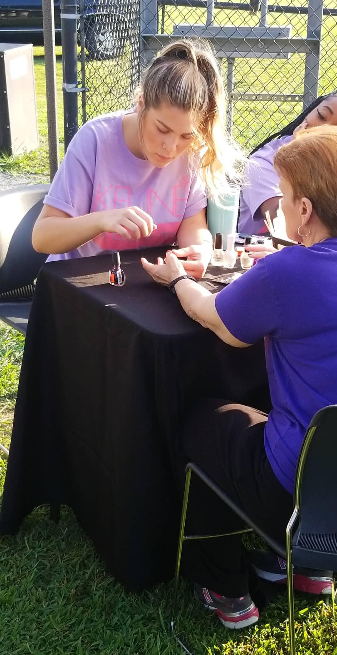 girl in purple shirt painting a woman's nails