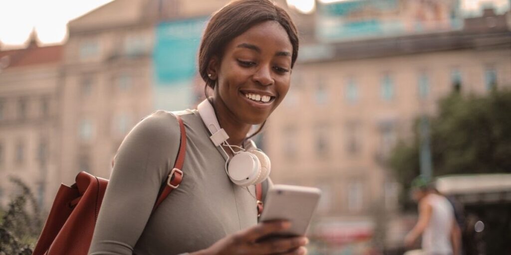 woman smiling and looking at her phone with a backpack on