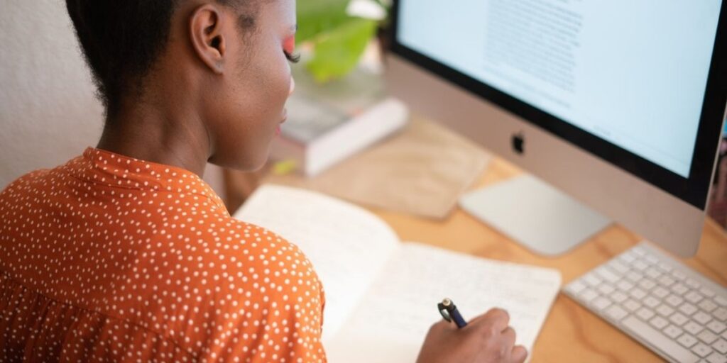 woman writing in a journal and looking at a computer