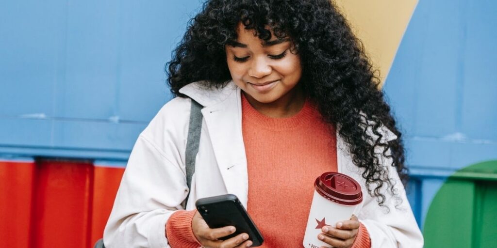 woman texting on her phone and holding a coffee cup